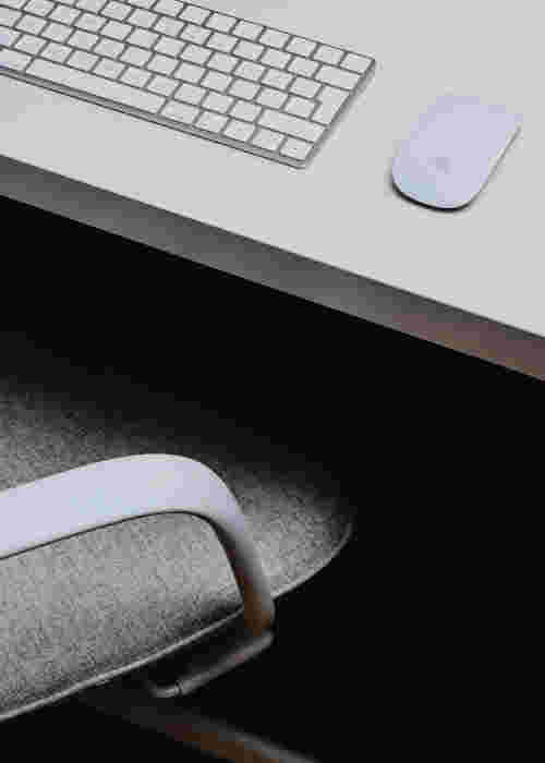 Utiliser un coussin lombaire au bureau pour améliorer sa posture Chaise de bureau avec clavier et souris sur un bureau blanc, idéale pour illustrer l’utilisation d’un coussin lombaire afin de soulager le dos en télétravail ou au poste de travail.