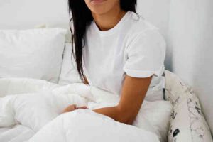 Utiliser un coussin lombaire au lit pour soulager le dos la nuit Femme assise dans son lit, en pyjama blanc, illustrant l’usage d’un coussin lombaire pour améliorer la posture et réduire les douleurs dorsales pendant le sommeil.
